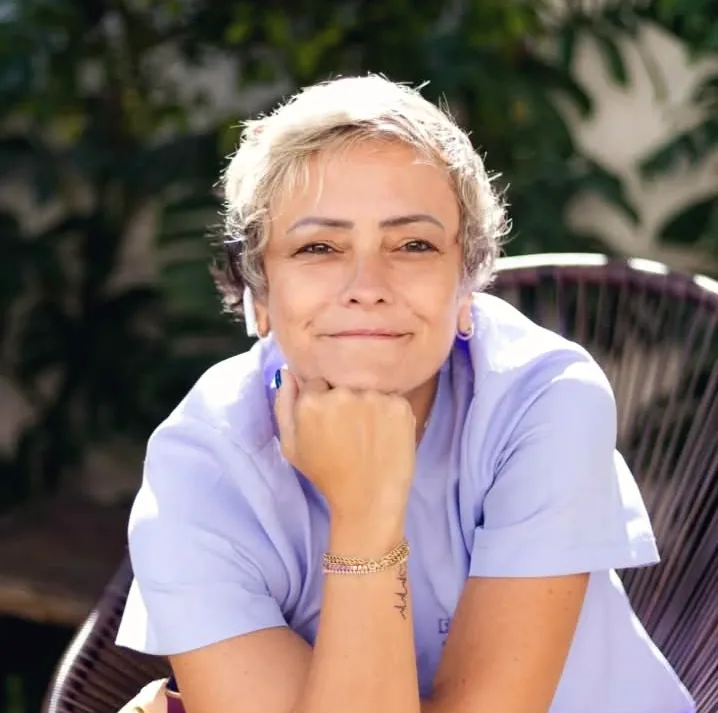 Lara Bueno, enfermeira e acupunturista, sentada e sorrindo, de jaleco lilás
